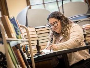 Lizbeth Santibanez works at a table surrounded by books in Rudisill Library